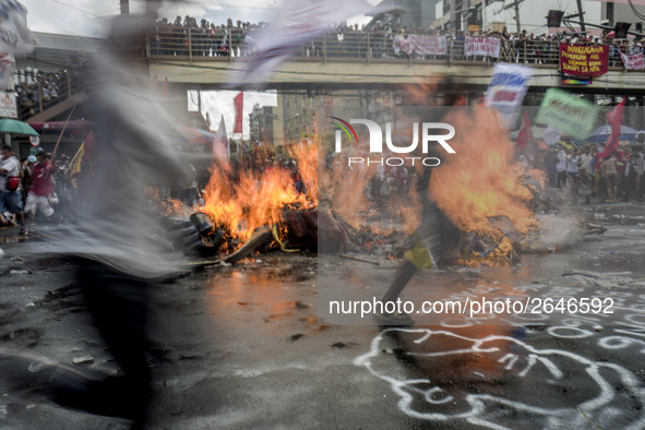 Workers run past a burning effigy of President Rodrigo Duterte as they take part in labor day demonstrations outside the presidential palace...