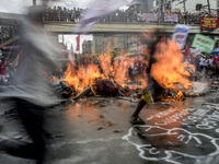 Workers run past a burning effigy of President Rodrigo Duterte as they take part in labor day demonstrations outside the presidential palace...