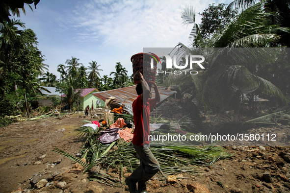 A man collects debris from a house damaged after a flood caused by damage to a river embankment after heavy rains in North Aceh, on November...