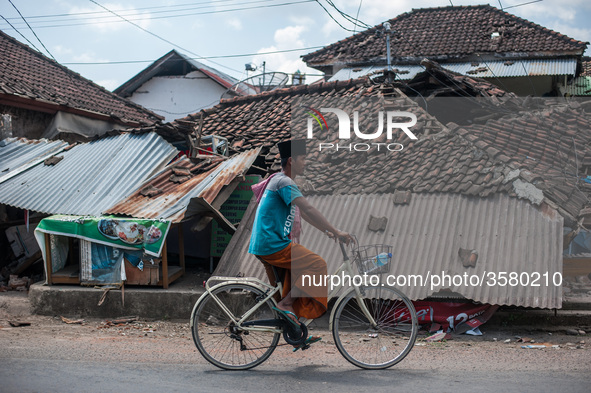 Cyclists pass through the ruins of houses due to earthquake on August 10, 2018 in Pamenang, North Lombok Regency, Indonesia. 