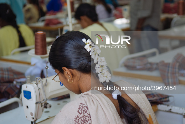 A seamstress wearing jasmine flowers in her hair working at a garment factory factory in Bangalore. Many of the workers emigrate from poor r...