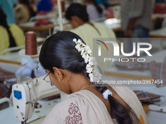 A seamstress wearing jasmine flowers in her hair working at a garment factory factory in Bangalore. Many of the workers emigrate from poor r...