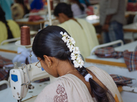 A seamstress wearing jasmine flowers in her hair working at a garment factory factory in Bangalore. Many of the workers emigrate from poor r...