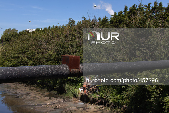 A man washes himself coming out of a pipe close to a factory. This water should end in the river behind him. It is hard to tell if the use o...