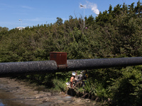 A man washes himself coming out of a pipe close to a factory. This water should end in the river behind him. It is hard to tell if the use o...