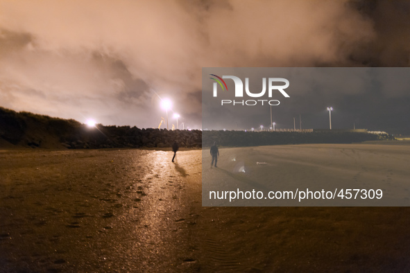 Two migrants walk along the beach approaching the barrier of rocks that separates de public area from the Ferri Port. Calais, France, June 2...