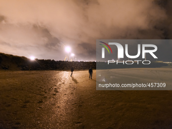 Two migrants walk along the beach approaching the barrier of rocks that separates de public area from the Ferri Port. Calais, France, June 2...