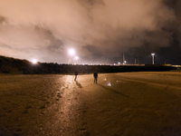 Two migrants walk along the beach approaching the barrier of rocks that separates de public area from the Ferri Port. Calais, France, June 2...