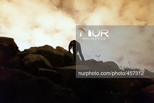 A migrant's body is silhouetted against the bright clouds bouncing light from the port's light posts as he climbs the rock that separate the...