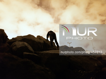 A migrant's body is silhouetted against the bright clouds bouncing light from the port's light posts as he climbs the rock that separate the...