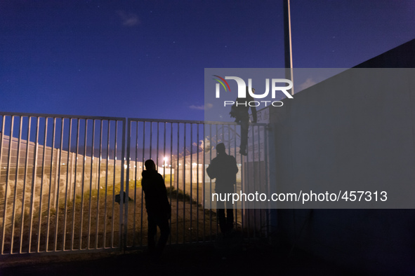 Three migrants start jumping the fences to access the port's truck parking lot. Calais, France, June 2014.

For the last 20 years the Fren...