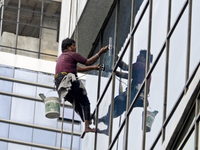 A worker cleans glass window of a building in Kolkata, India, 24 July, 2019  (