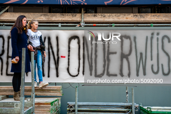 A woman and her daughter are seen in front of a big banner where can red it the word Onderwijs, which means education in Dutch during the ma...