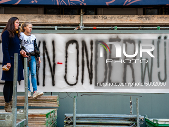 A woman and her daughter are seen in front of a big banner where can red it the word Onderwijs, which means education in Dutch during the ma...