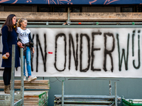 A woman and her daughter are seen in front of a big banner where can red it the word Onderwijs, which means education in Dutch during the ma...