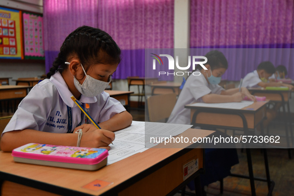 Elementary school students wearing face masks in social distancing as a preventive measure in a class is a demonstration of learning amid th...