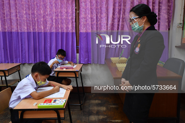 Elementary school students wearing face masks and a teacher wearing a face shield in social distancing as a preventive measure in a class is...