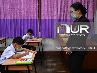 Elementary school students wearing face masks and a teacher wearing a face shield in social distancing as a preventive measure in a class is...