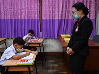 Elementary school students wearing face masks and a teacher wearing a face shield in social distancing as a preventive measure in a class is...