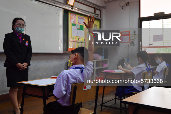 Elementary school students wearing face masks and a teacher wearing a face shield in social distancing as a preventive measure in a class is...