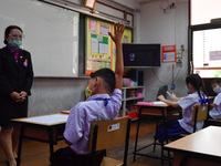 Elementary school students wearing face masks and a teacher wearing a face shield in social distancing as a preventive measure in a class is...