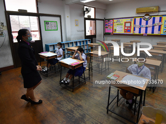 Elementary school students wearing face masks and a teacher wearing a face shield in social distancing as a preventive measure in a class is...