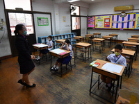 Elementary school students wearing face masks and a teacher wearing a face shield in social distancing as a preventive measure in a class is...