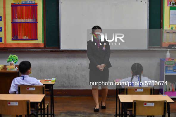 Elementary school students wearing face masks and a teacher wearing a face shield in social distancing as a preventive measure in a class is...