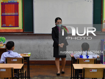 Elementary school students wearing face masks and a teacher wearing a face shield in social distancing as a preventive measure in a class is...