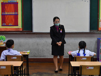 Elementary school students wearing face masks and a teacher wearing a face shield in social distancing as a preventive measure in a class is...