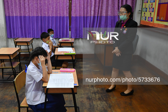 Elementary school students wearing face masks and a teacher wearing a face shield in social distancing as a preventive measure in a class is...