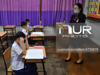 Elementary school students wearing face masks and a teacher wearing a face shield in social distancing as a preventive measure in a class is...