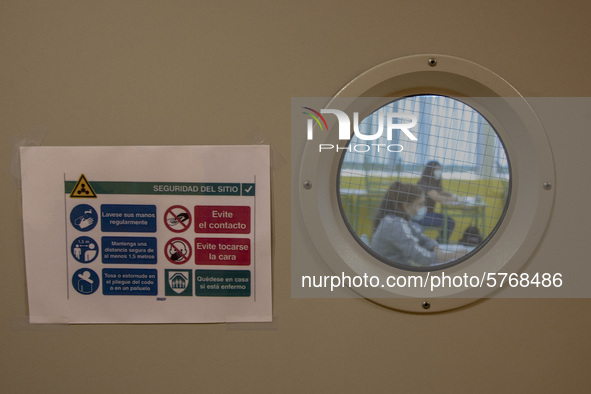 Two students receive a refresher class through a window with a sign indicating the sanitary rules to follow to avoid the coronavirus in Nore...