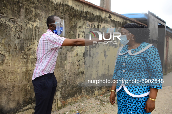 A High school teacher wear a face mask as she check temperature of a Permanent Secretary Education District III, Dr Yinka Ayandele, with inf...