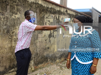 A High school teacher wear a face mask as she check temperature of a Permanent Secretary Education District III, Dr Yinka Ayandele, with inf...