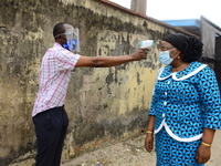 A High school teacher wear a face mask as she check temperature of a Permanent Secretary Education District III, Dr Yinka Ayandele, with inf...