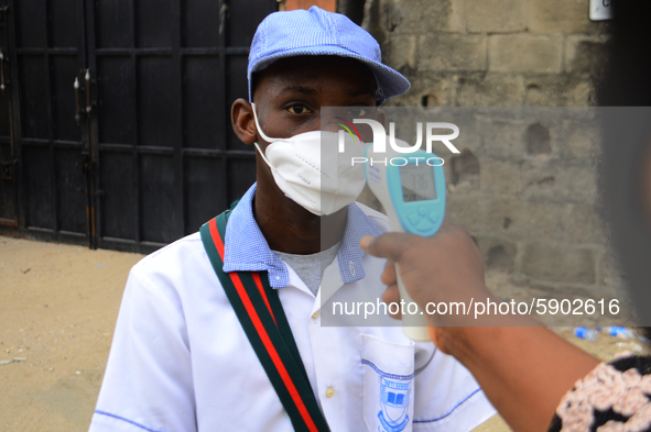 A High school teacher wear a face mask as he check temperature of a student with infrared tool at the entrance of Ireti Junior Grammar Schol...