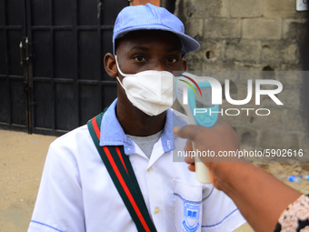 A High school teacher wear a face mask as he check temperature of a student with infrared tool at the entrance of Ireti Junior Grammar Schol...