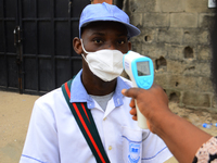 A High school teacher wear a face mask as he check temperature of a student with infrared tool at the entrance of Ireti Junior Grammar Schol...