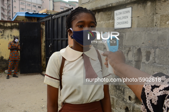 A High school teacher wear a face mask as he check temperature of a student with infrared tool at the entrance of Ireti Junior Grammar Schol...