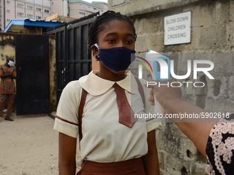 A High school teacher wear a face mask as he check temperature of a student with infrared tool at the entrance of Ireti Junior Grammar Schol...