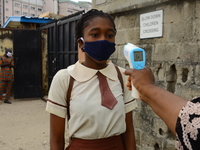 A High school teacher wear a face mask as he check temperature of a student with infrared tool at the entrance of Ireti Junior Grammar Schol...