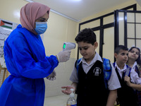 A Palestinian staff member checks a student temperature in the rosary sisters school gaza , on the first day of a new school year, as Palest...