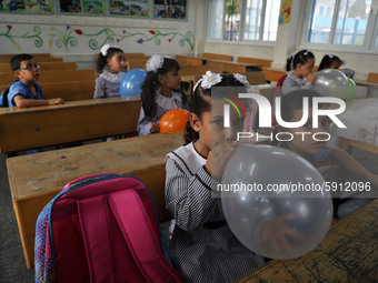 Palestinian students holding balloons sit in a classroom at a United Nations-run school as a new school year begins as Palestinians ease the...