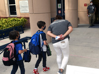 A  school employee escorts children as they return to school on the first day of in-person classes in Orange County at Baldwin Park Elementa...