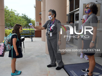 A school employee checks the temperature of a student as she returns to school on the first day of in-person classes in Orange County at Bal...