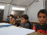 Syrian students wearing protective masks sit on their seats during the first day of the school year in a camp for displaced people near the...