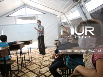 Syrian students wearing protective masks sit on their seats during the first day of the school year in a camp for displaced people near the...