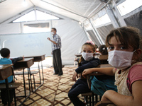 Syrian students wearing protective masks sit on their seats during the first day of the school year in a camp for displaced people near the...