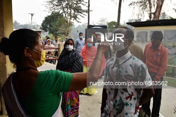 A health worker checks the body temperature of a voter, as a preventive measure against the COVID-19 coronavirus, before casting her ballot...